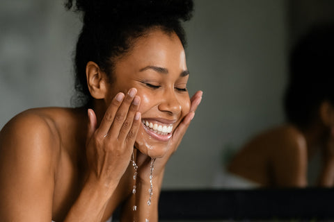 Woman smiling while cleansing her face — representing natural, organic face cleansers for sensitive skin by Conscious Skincare.