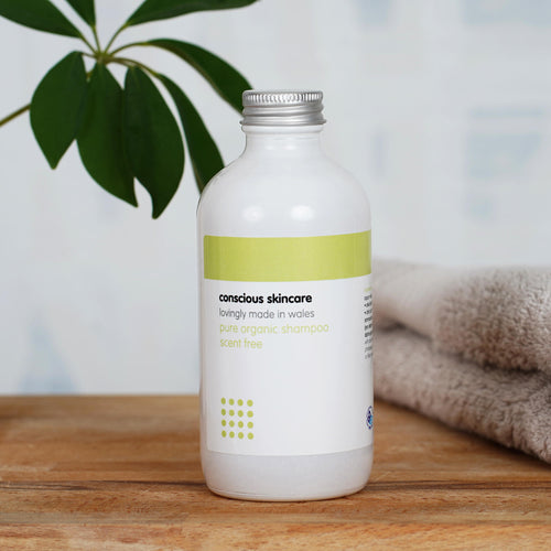 Pure Fragrance Free Shampoo in a white glass bottle on a wooden table with towel