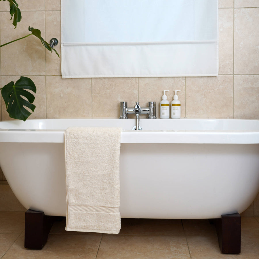 organic hand towel placed on side of white bath in bathroom setting