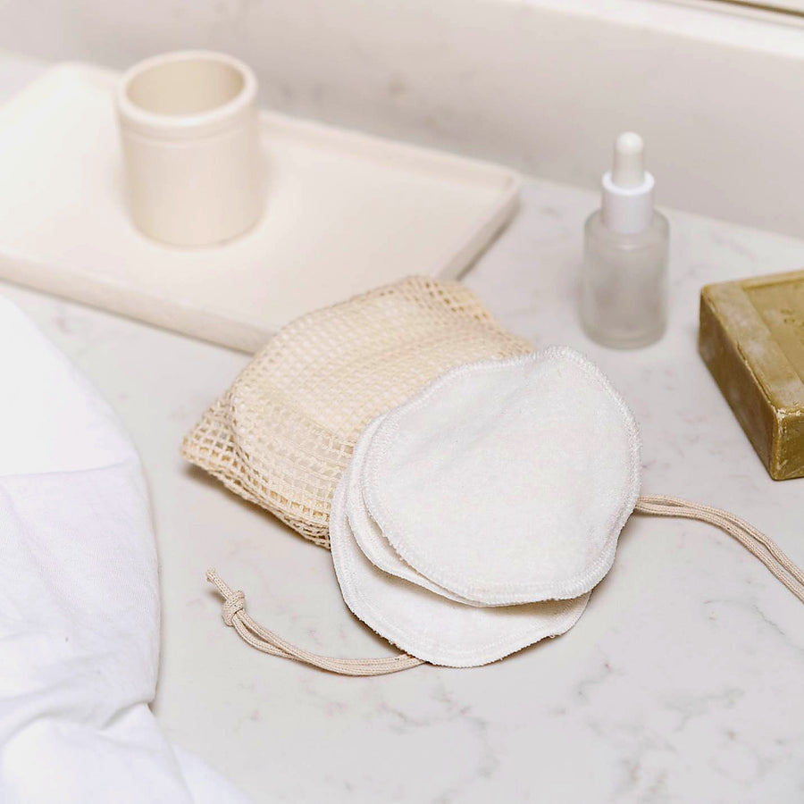 Organic cotton reusable makeup pads arranged by mesh wash bag, minimal bathroom setting,