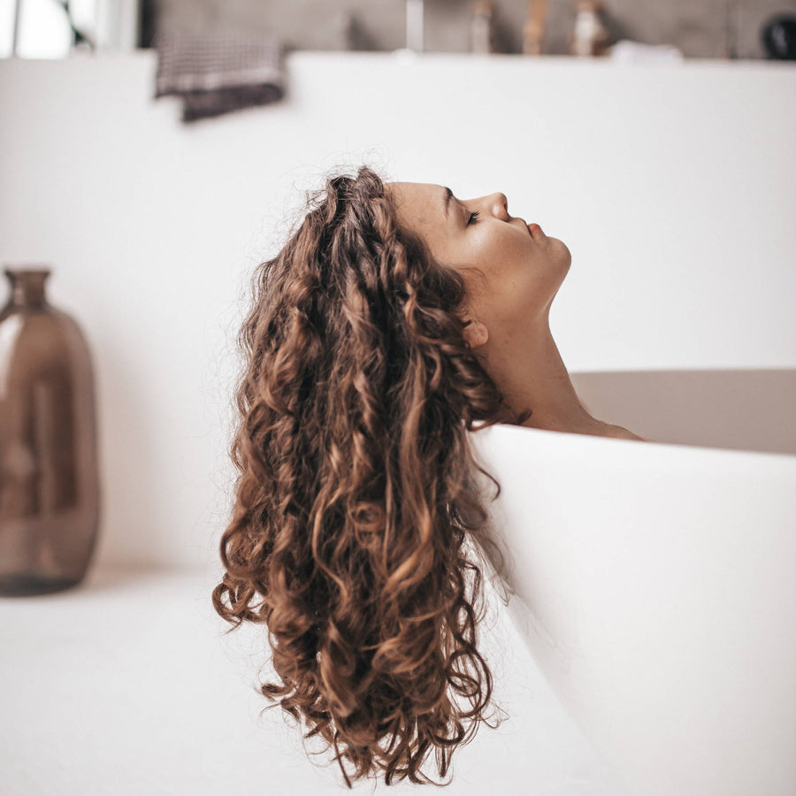 Organic Bath Soak - woman relaxing in white bath with long brown curly hair