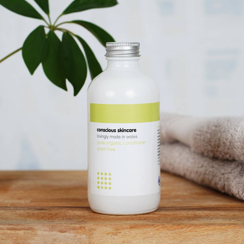 Organic Conditioner in a white glass bottle with silver cap on wooden table with plant and towel