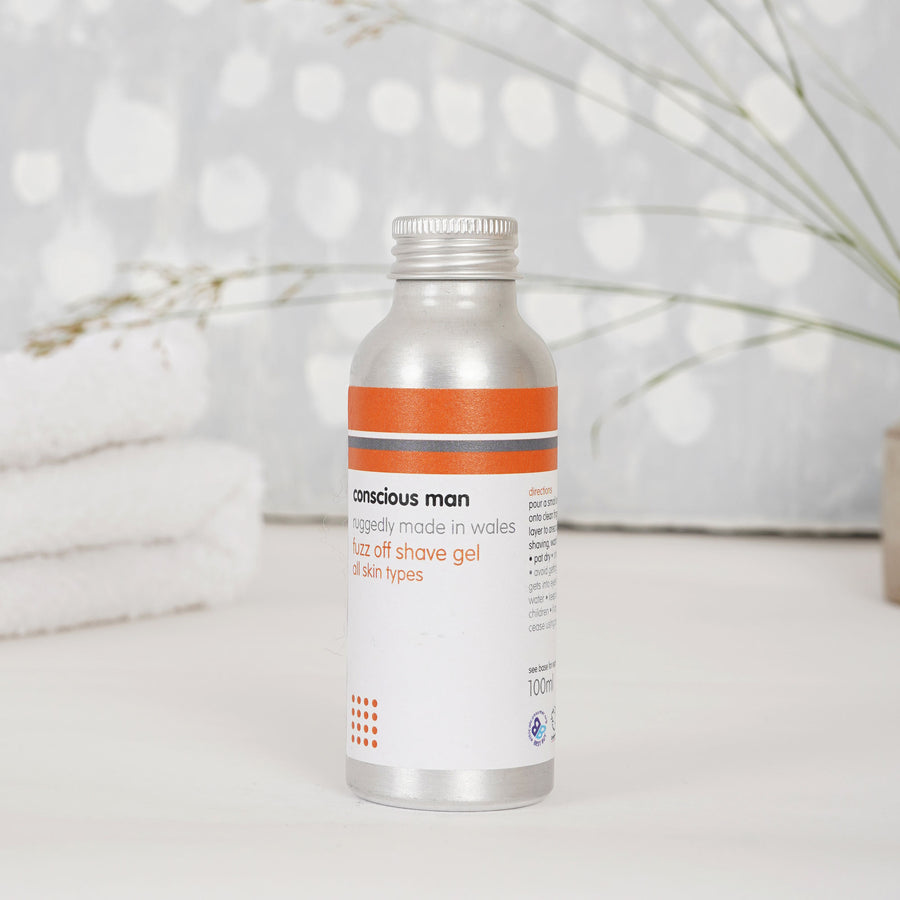 Lifestyle image of Fuzz Off shaving gel with towels and greenery — fresh citrus-herbal finish from lemon balm and lemongrass.