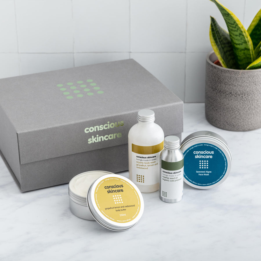 Conscious Skincare grey gift box with 4 organic skincare products on a white table with plant 